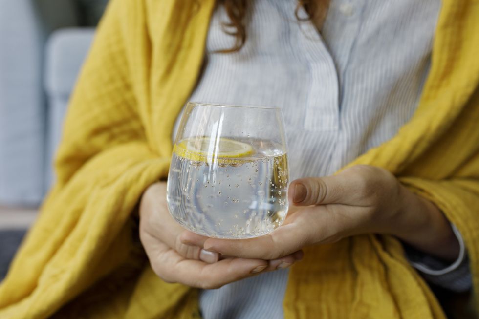 woman's hands holding sparkling water with lemon slice in glass
