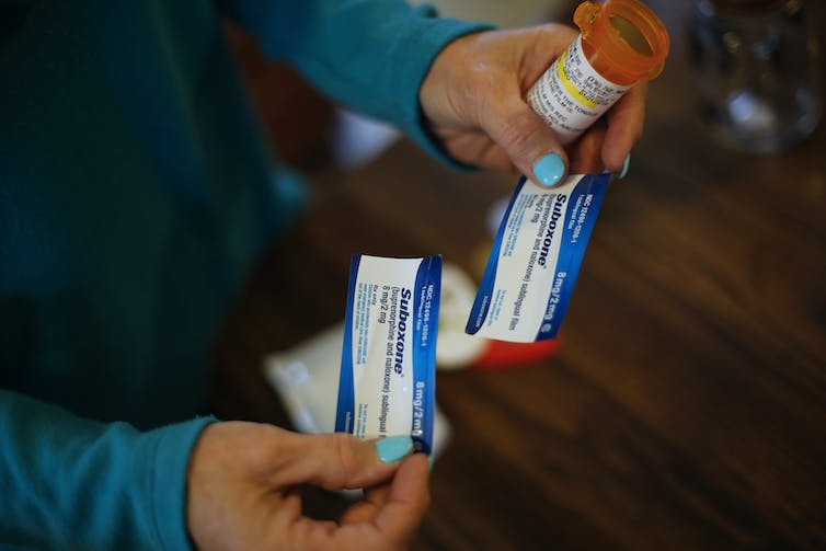 Close-up photo of a woman's hands holding two small packets labeled Suboxone.